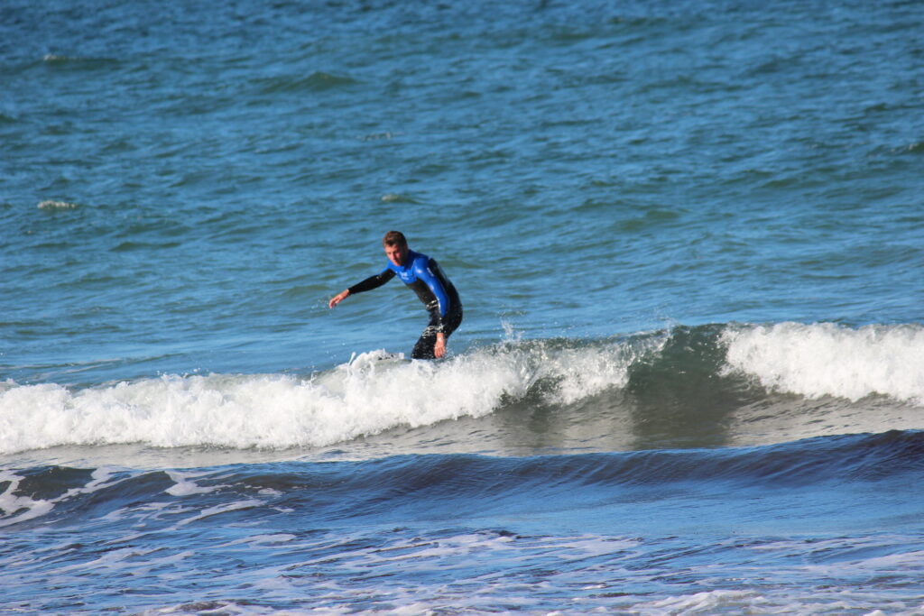 Homme en combinaison bleue et noire surfant une petite vague sur la côte bretonne près de Quiberon