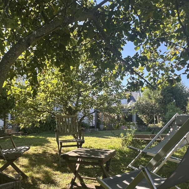 Salon de jardin en bois et transats ombragés sous les pommiers du verger du Clos Kerhadenn